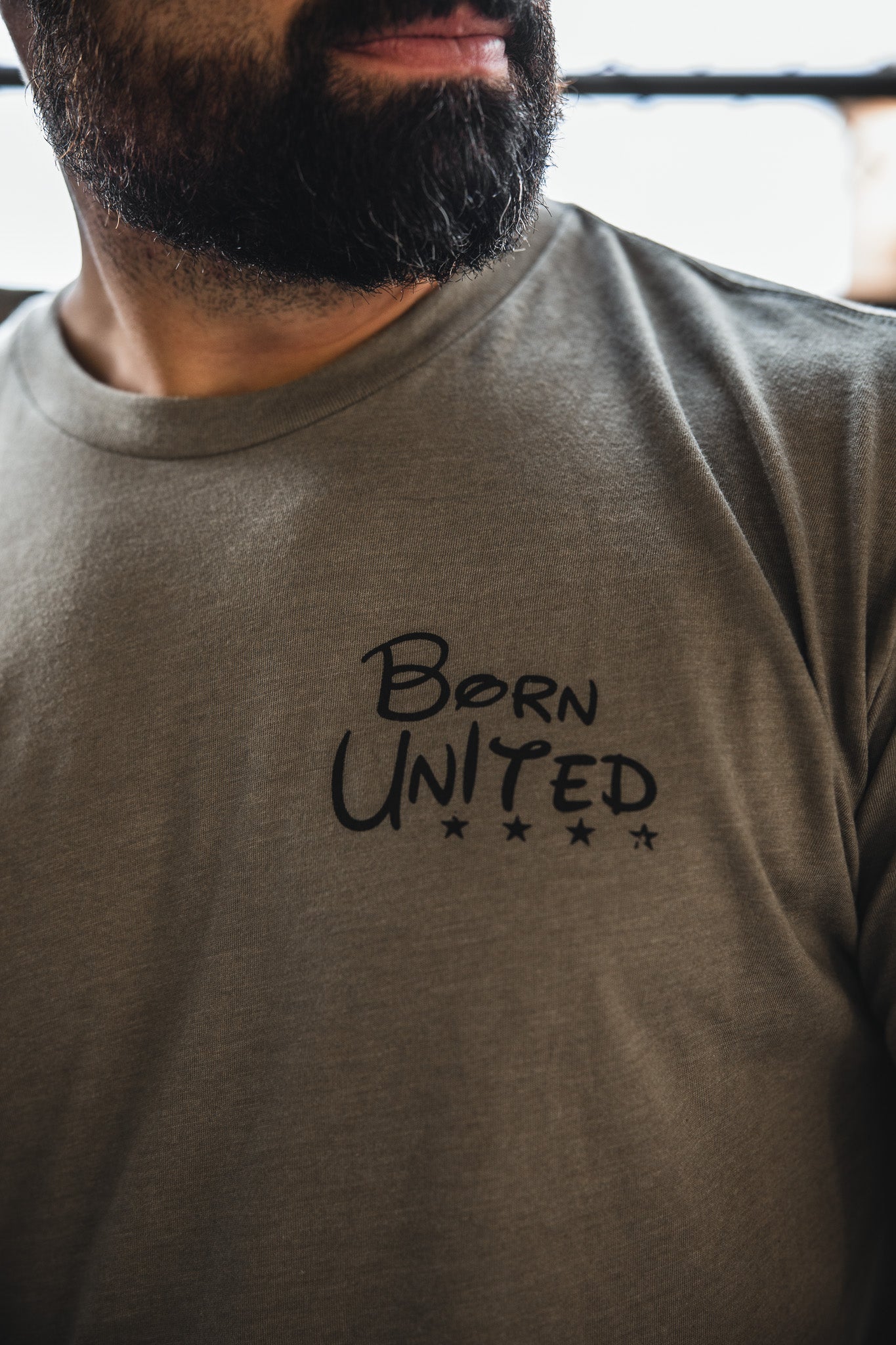 A close-up of a bearded man in a gray "Triggered" t-shirt from Born United Private Label, featuring bold black letters that embody American patriotism.