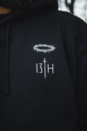 Close-up of the Jesus Saves Hoodie by 13th: a black Christian hoodie with a white crown of thorns above "13TH," the T as a sword—merging bold faith and striking design.