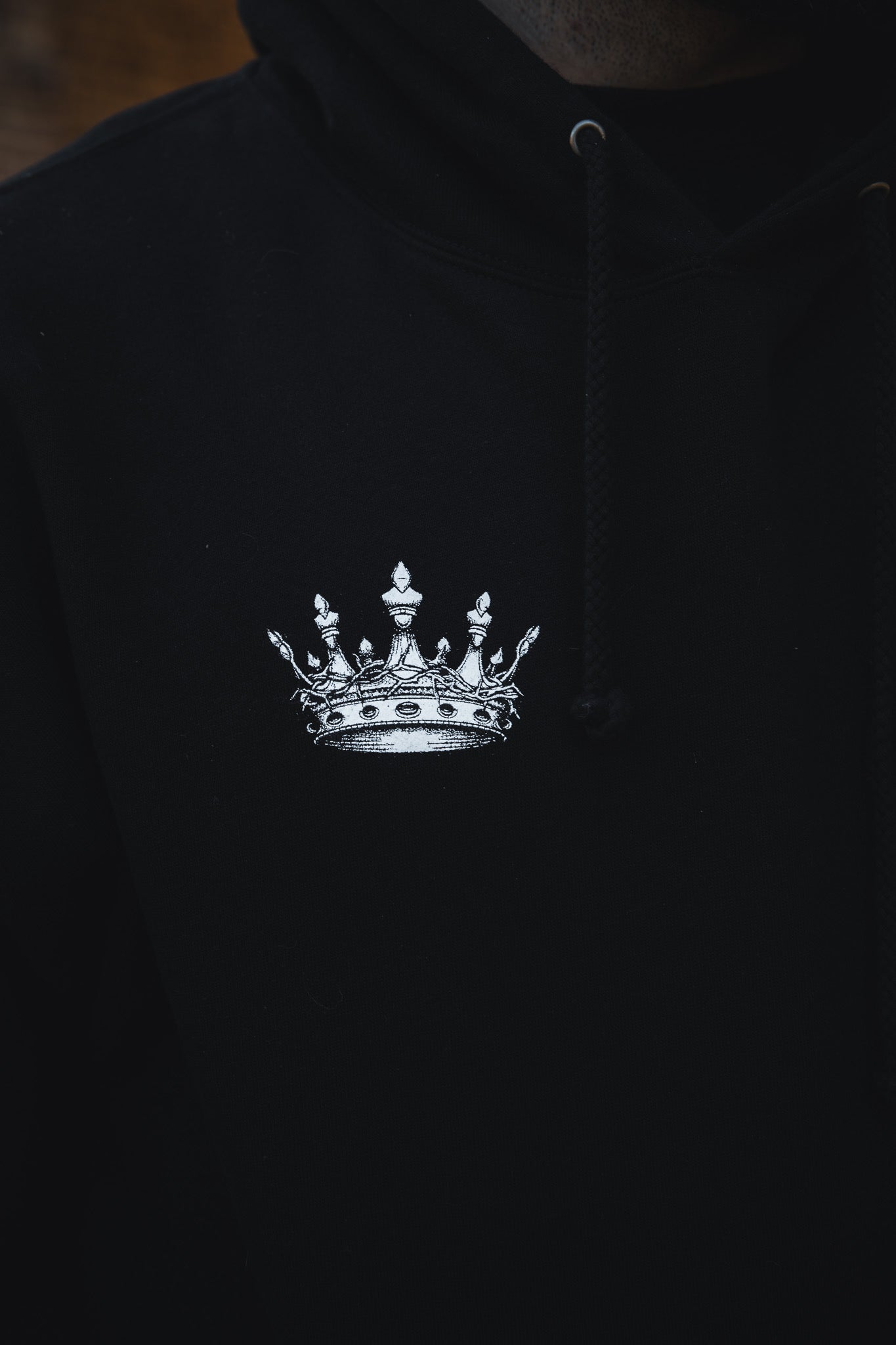 A close-up of the 13th Christ is King Premium Hoodie shows a detailed white crown graphic on the chest, visible drawstrings, and a dark background.