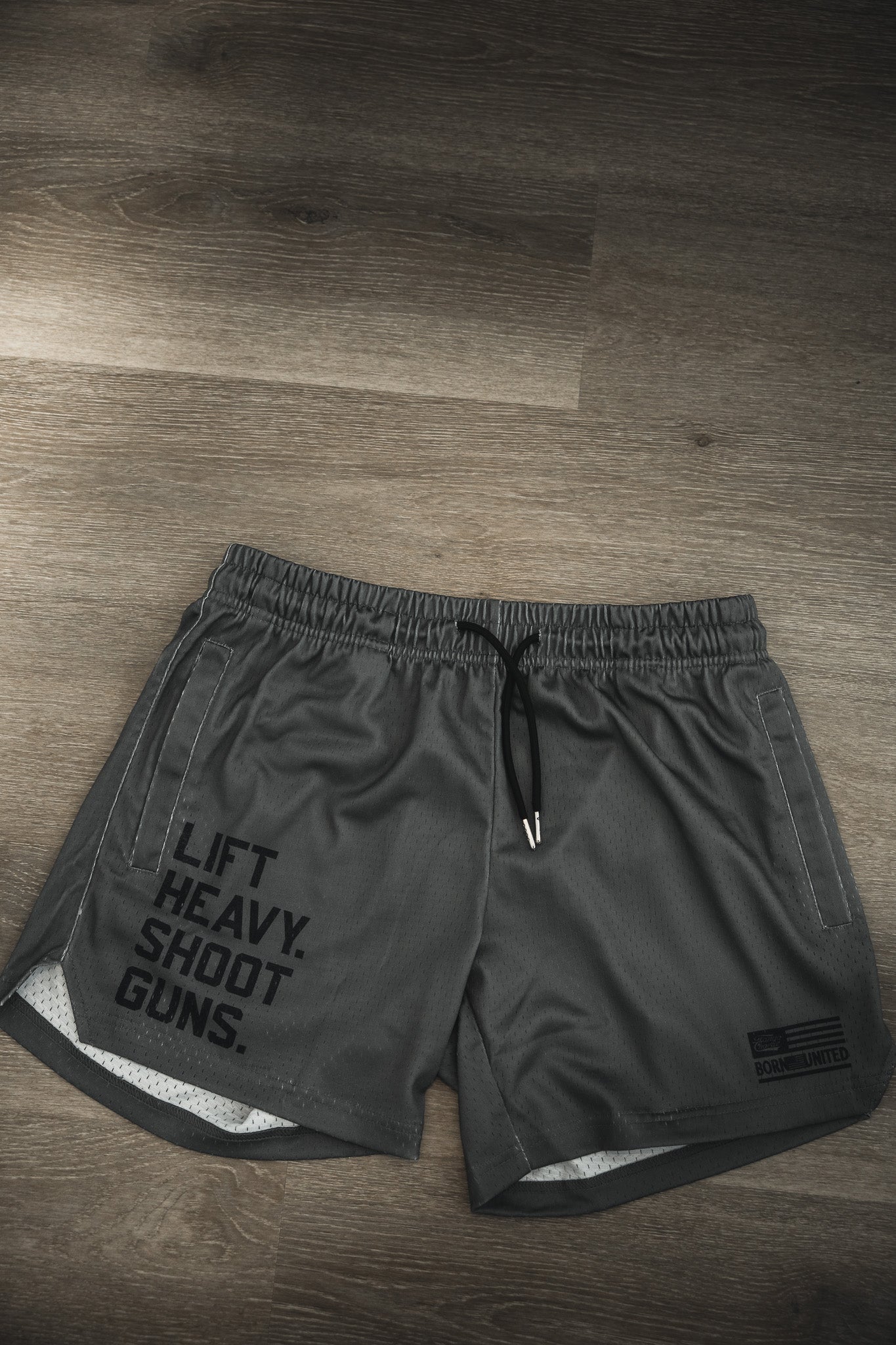 A pair of LHSG OD Green men’s mesh lifestyle shorts by Tango Charlie Apparel with a black drawstring, 5.5" inseam, and bold "LIFT HEAVY. SHOOT GUNS." print on the left leg—perfect for athletic or casual wear.