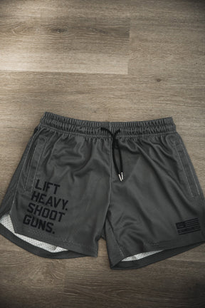 The Tango Charlie Apparel Men's Mesh Lifestyle Shorts | 5.5"- LHSG OD Green feature bold "LIFT HEAVY. SHOOT GUNS." text on the left leg, black drawstrings, and are perfect for workouts or everyday wear.