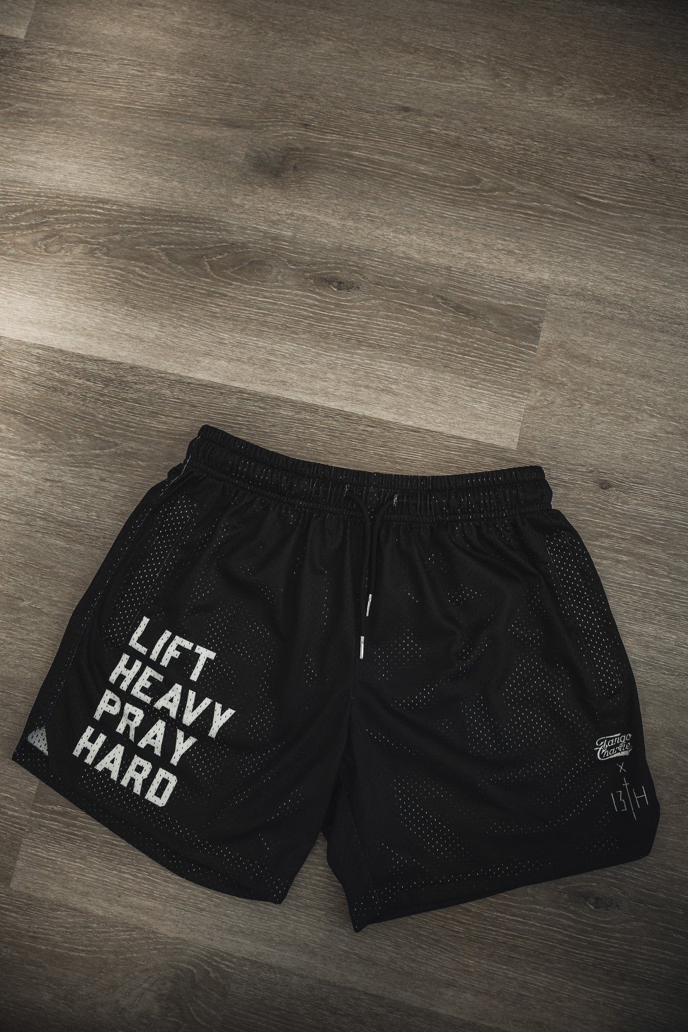 Tango Charlie Apparel Men's Mesh Lifestyle Shorts | 5.5" - Lift Heavy Pray Hard Black: Black quick-dry gym shorts with "LIFT HEAVY PRAY HARD" in white on the left leg, designed for men’s comfort during intense workouts.