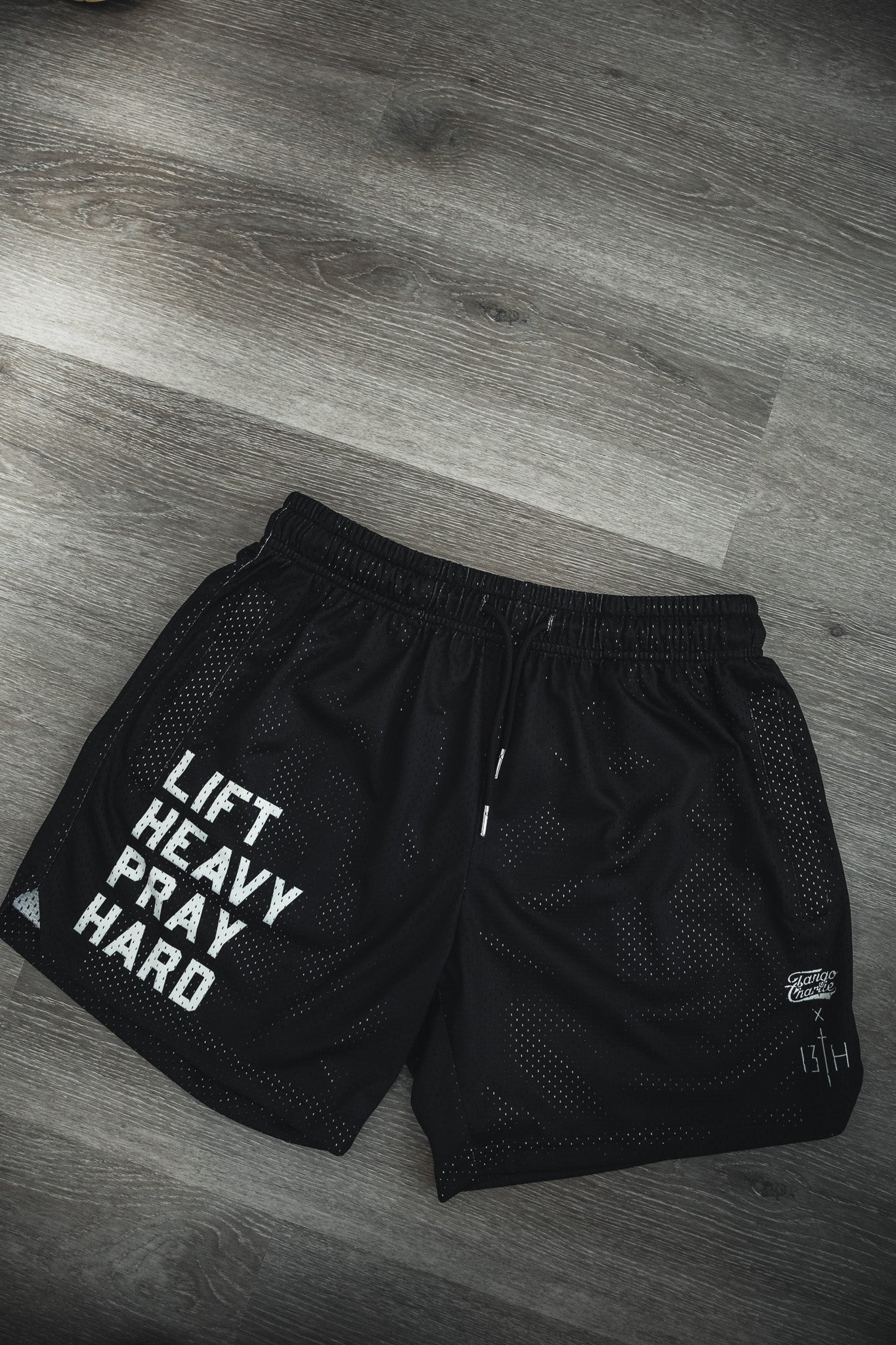 Tango Charlie Apparel's Men's Mesh Lifestyle Shorts | 5.5" in black feature "LIFT HEAVY PRAY HARD" text and a 13TH logo—perfect gym shorts for workouts or everyday wear.