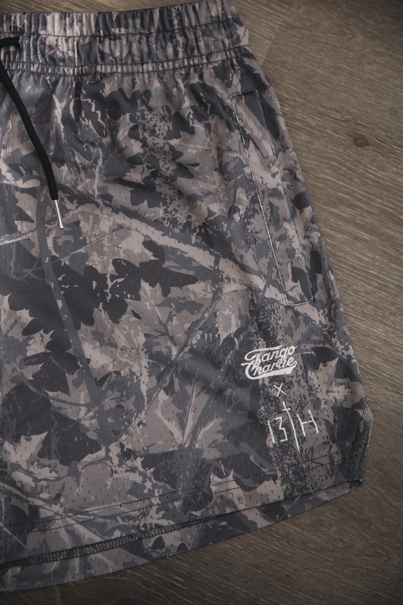 Men's Mesh Lifestyle Shorts | 5.5" - Lift Heavy Pray Hard Deadwood by Tango Charlie Apparel, shown in gray camo with a black drawstring, Rango Charlie logo, and two white symbols near the hem—great for everyday wear.