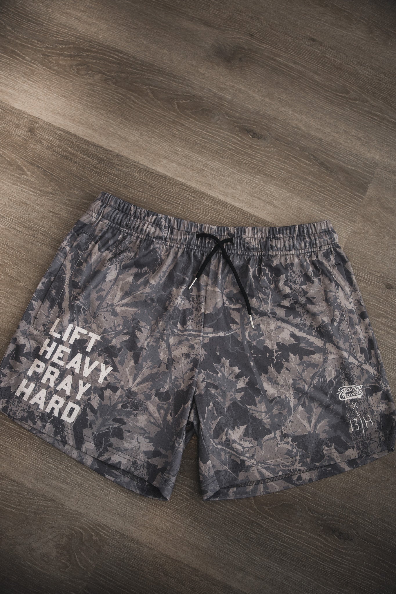 The Tango Charlie Apparel Men's Mesh Lifestyle Shorts | 5.5"- Lift Heavy Pray Hard Deadwood feature gray camo, black drawstrings, and "LIFT HEAVY PRAY HARD" in white—perfect mesh shorts for an active lifestyle.