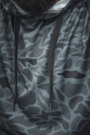 Close-up of the Mucker Bucket Performance Hoodie - Stealth Camo, featuring a gray and black abstract camo pattern with black drawstrings. A portion of a persons beard is visible at the top of the image.
