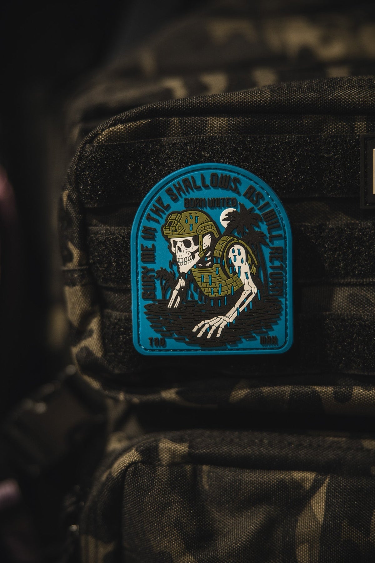 The Born United Private Label The Shallows PVC Patch features a skeleton in military gear rising from water on a camouflage backpack, with the phrase Down in the shallows rise the legends.