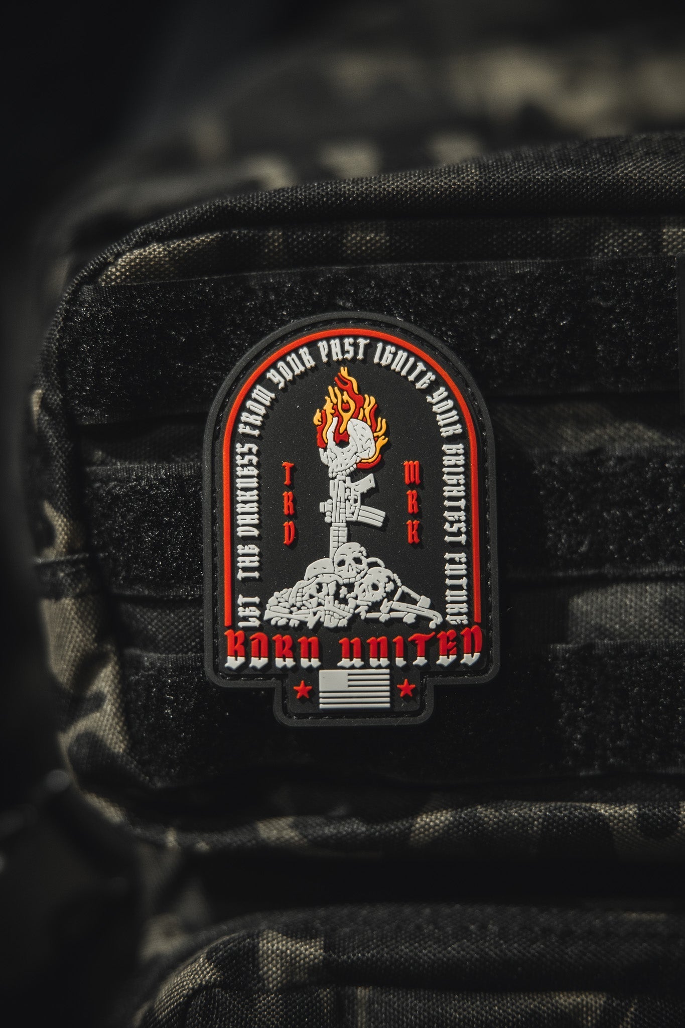 The Let The Darkness PVC Patch by Born United Private Label features a fiery torch above skulls and bones with BORN UNITED and phrases encircling the torch, all set on textured black fabric.