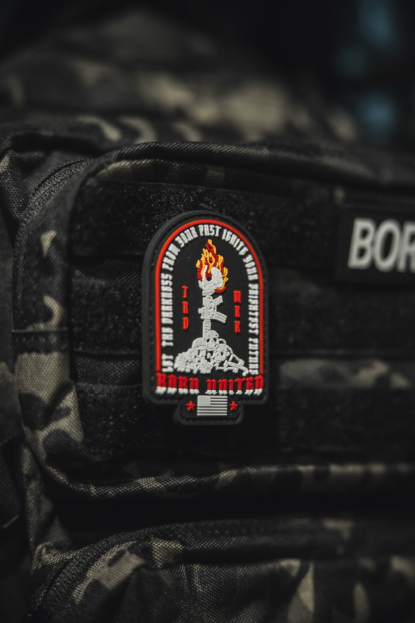 A close-up of a black camo backpack shows the Let The Darkness PVC patch by Born United Private Label, featuring a flaming torch, skull, “HARD UNITED” in red, plus smaller text and symbols. A BORN label appears above the patch.