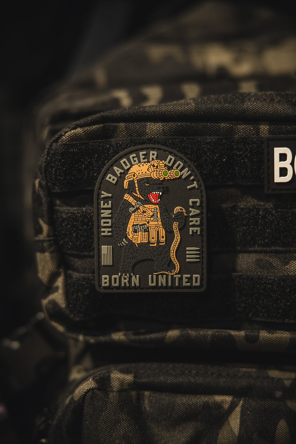 The Honey Badgerin PVC Patch by Born United Private Label features a cartoon armored honey badger with a rifle and the phrases “HONEY BADGER DON’T CARE” and “BORN UNITED.”.