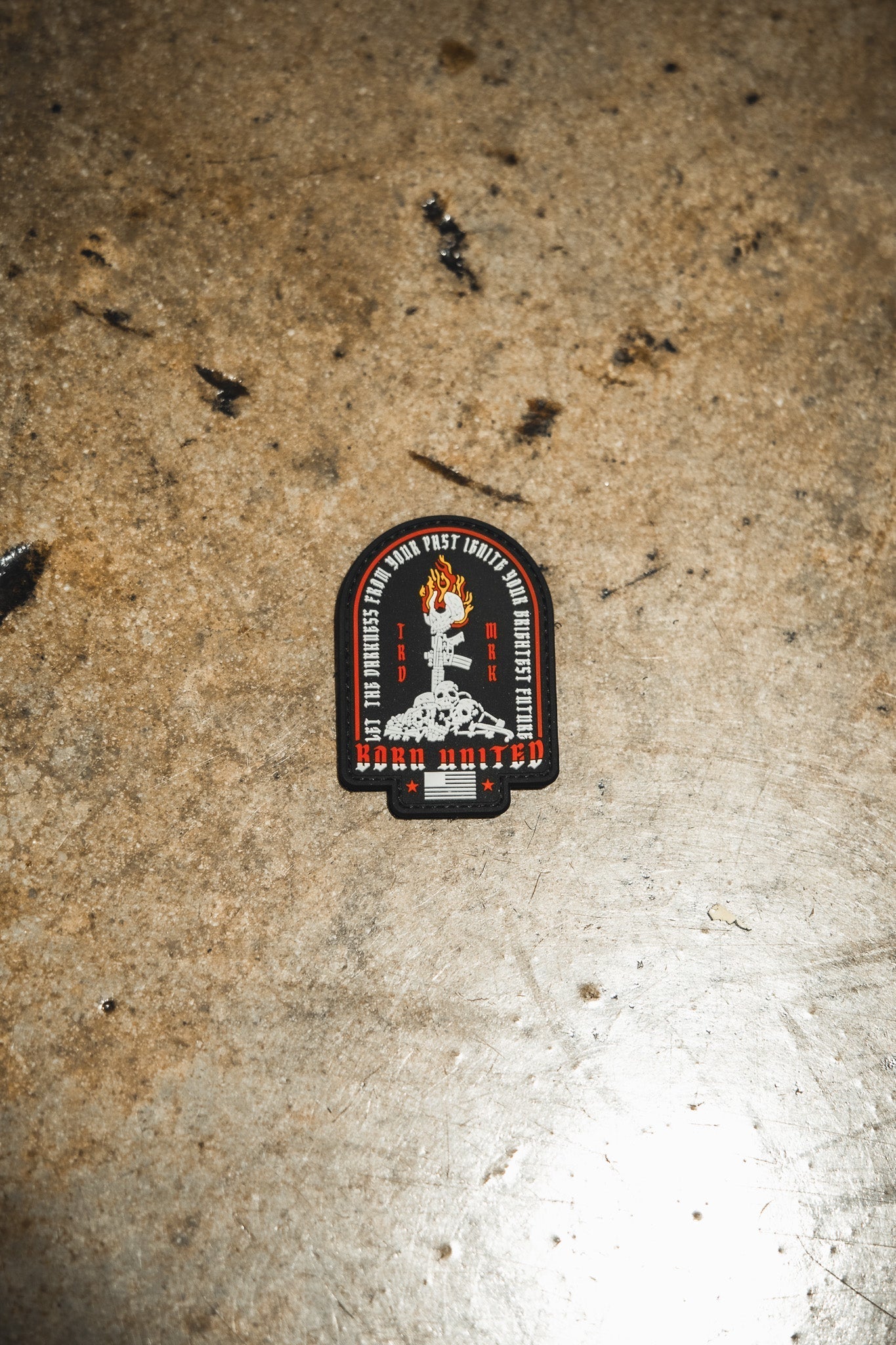 The Let The Darkness PVC Patch by Born United Private Label features a raised fist with a wrench, surrounded by text and “Work United” at the bottom in red, black, and white on a rugged brown surface.
