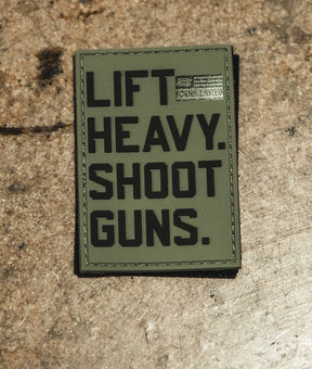 The Lift Heavy. Shoot Guns. - PVC Patch by Tango Charlie Apparel has bold black text on a green, textured surface with a small American flag in the top right corner.