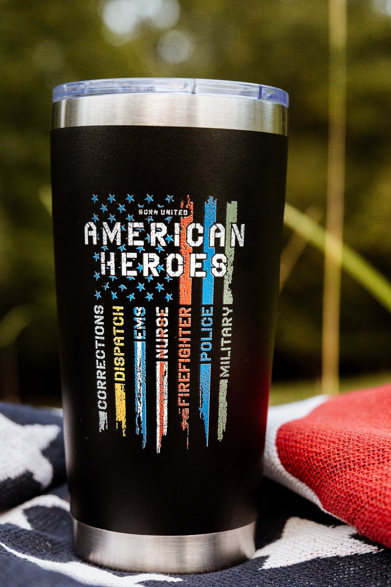 The Born United Private Label American Heroes Tumbler - 20oz showcases colored stripes and “Born United American Heroes” with Corrections, Dispatch, Nurses, Firefighter, Police, and Military on a star-patterned blanket.