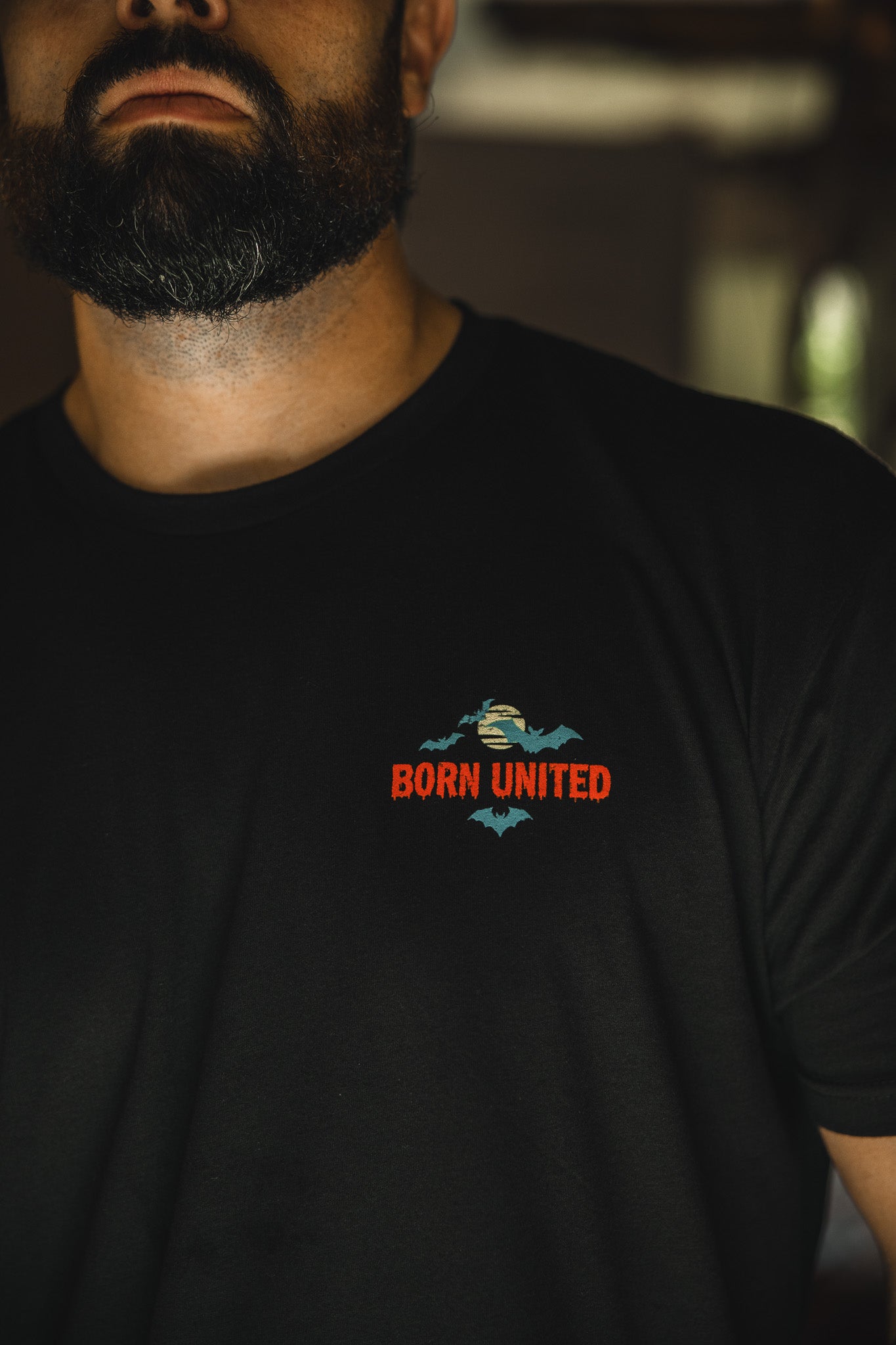 A dark-bearded man wears the Count Tacula limited edition Halloween shirt by Born United Private Label, featuring a small embroidered bat design and "BORN UNITED" in red and orange on the left chest. The image is cropped at his chin.