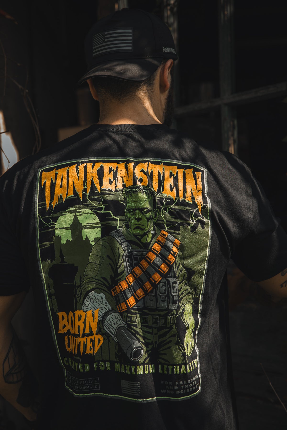 A man in a black cap and Tankenstein T-shirt by Born United Private Label stands with his back to the camera; the exclusive shirt displays a Frankenstein-like soldier graphic with "TANKENSTEIN" and "Born United" text.