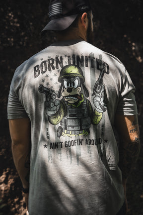 A man wearing a cap faces away, showing the "Ain't Goofin' Around" T-shirt by Born United Private Label, with a cartoon dog in military gear holding pistols. “BORN UNITED” is above and “AIN'T GOOFIN' AROUND” is boldly below the image.