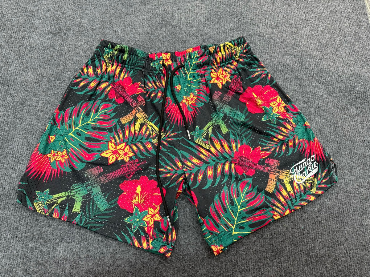 The Tango Charlie Apparel Men's Mesh Lifestyle Shorts | 5.5"- Tropical Assassin feature a tropical floral design with green leaves, vibrant flowers, black drawstring, and white logo—lightweight, quick-dry shorts for stylish comfort. Laid flat on gray carpet.