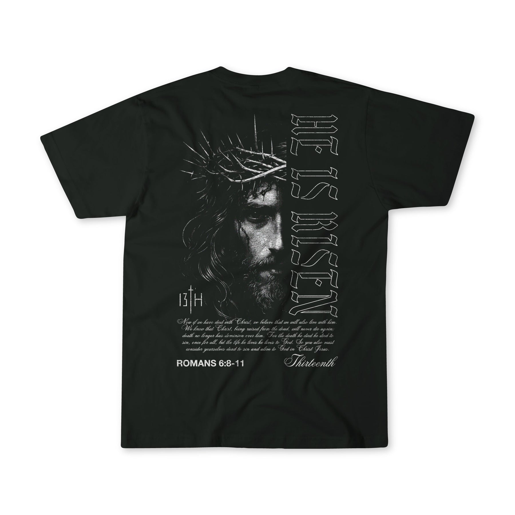 The 13th He is Risen Premium Tee is a black shirt showcasing an illustrated Jesus with a crown of thorns on the back, plus “HE IS RISEN,” Romans 6:8-11, and bold Christian text.