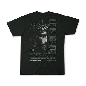 The 13th He is Risen Premium Tee is a black shirt showcasing an illustrated Jesus with a crown of thorns on the back, plus “HE IS RISEN,” Romans 6:8-11, and bold Christian text.