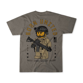 The Brick Operator-Youth tee by Born United Private Label is a gray shirt with a LEGO-style soldier in tactical gear and rifle. BORN UNITED arcs above, with a black American flag, stars, and BUILD • SHOOT • DESTROY • RELOAD below.
