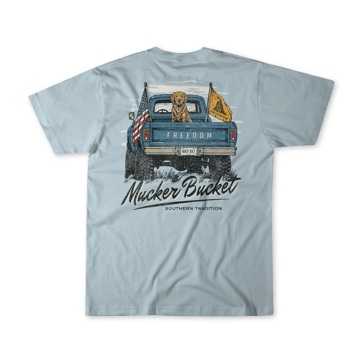 The Lab Truck Premium Tee by Mucker Bucket showcases a light blue design with a graphic of a dog in a truck bed, two flags, and the word “FREEDOM” on the front, while “Mucker Bucket Southern Tradition” is featured on the back. Crafted from soft ring-spun cotton for all-day comfort, this relaxed fit tee embodies classic Southern style.