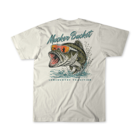 Introducing the Cool Bass Premium Tee by Mucker Bucket—a white t-shirt featuring a striking graphic of a leaping fish in orange sunglasses. “Mucker Bucket” is printed above the image, with “Lowcountry Tradition” below. Made from soft ring-spun cotton for a relaxed fit, this stylish tee seamlessly blends comfort and coastal vibes.