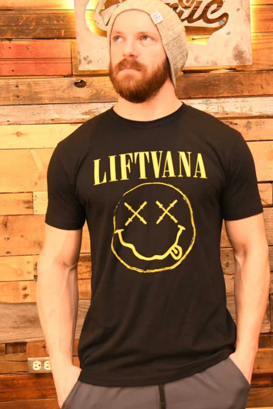 A man and woman stand before a wooden wall, both in black "Liftvana" Men's Tees by Tango Charlie Apparel featuring a yellow graphic. Their serious looks and the man's beanie add grunge energy, reflecting the true lifter’s spirit.