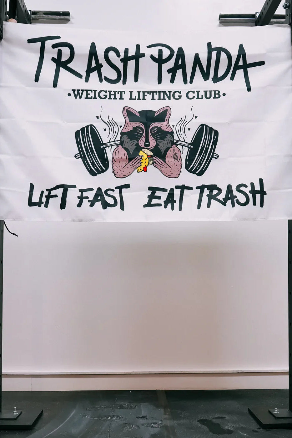 The Trash Panda - Flag by Tango Charlie Apparel is a 3x5 polyester banner featuring a raccoon lifting barbells and eating pizza, with "Trash Panda Weight Lifting Club" and "Lift Fast Eat Trash"—perfect for your squat rack or gym wall.