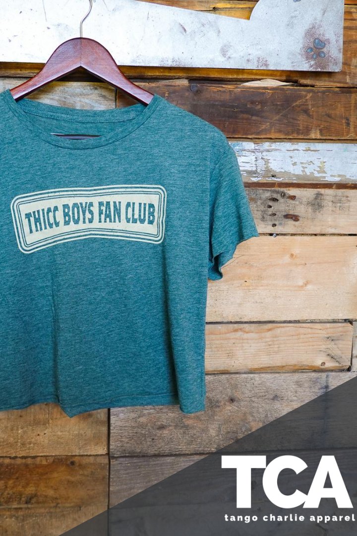 The green THICC Boys Fan Club Crop Tee by Tango Charlie Apparel features bold lettering and a white TCA logo with "tango charlie apparel" below—an ideal choice for dadbods who want to show off their pride.